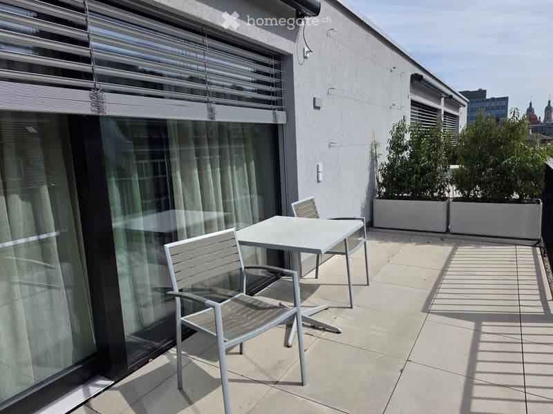 Outdoor balcony with a table and chairs, large windows, and potted plants.