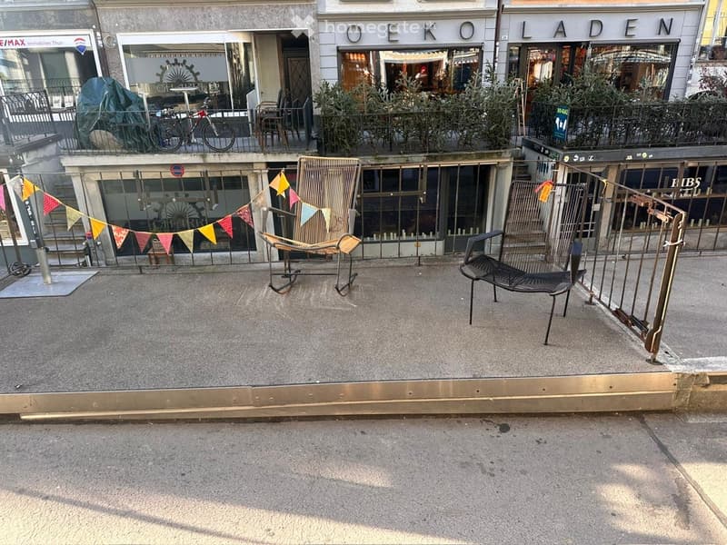 outside, cafe chairs, metal railings, stairs, flags hanging, plants on balcony