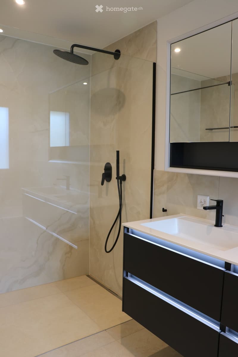 Marble walls, modern shower, white countertop, black cabinet, white sink, electrical outlet