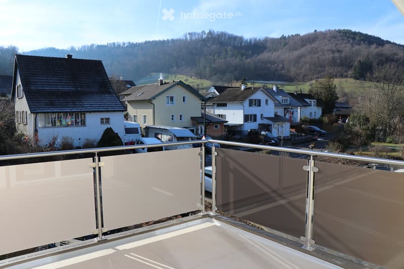 Terrace with a metal railing, white screens, view of a village with houses in the background, mountain
