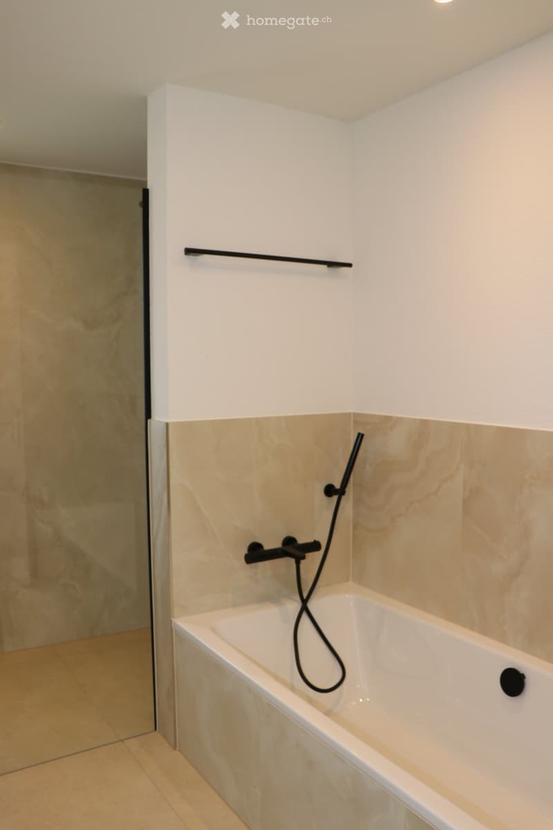 large bathtub, shower head on wall, marble walls, no cabinet