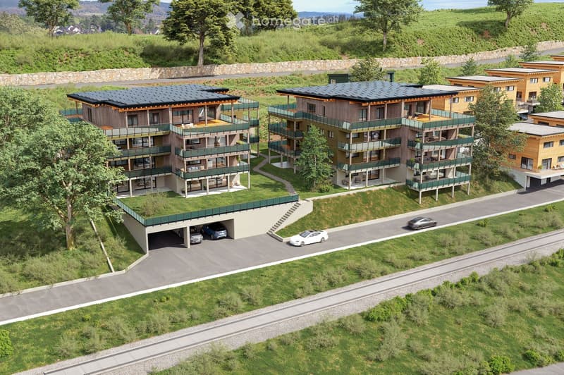 Aerial view of modern multi-storey apartment buildings with car parking, green spaces, and a view of a mountain range.