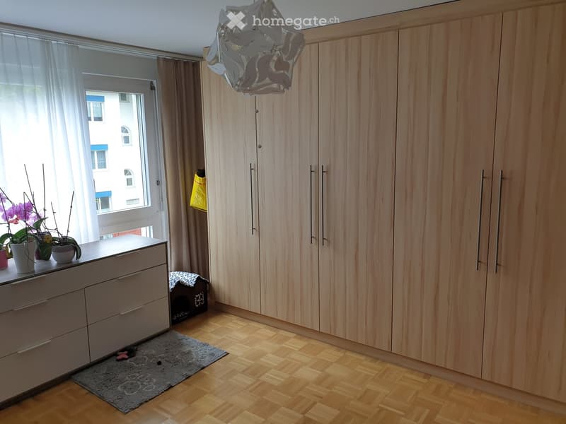wooden wardrobes, wooden floors, white dresser, rug, window with white curtains, flowers in pots on dresser