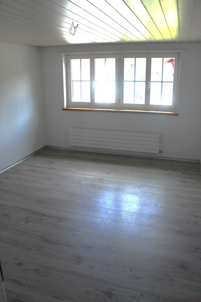 empty room, white walls, gray wooden floor, windows, radiator, lights on the ceiling