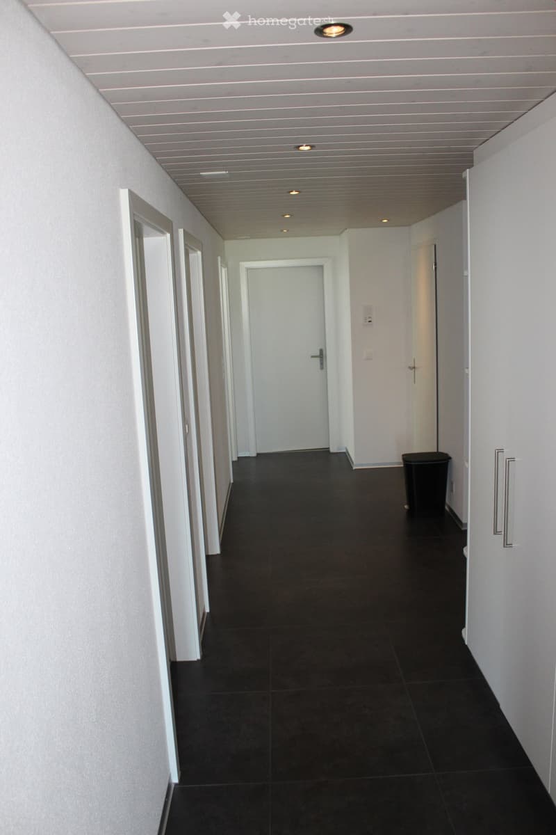corridor with black tiles, white walls, doors on either side, light ceiling