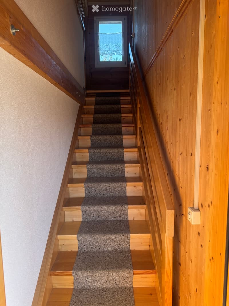 Wooden stairs leading to a door, wooden handrail, white wall