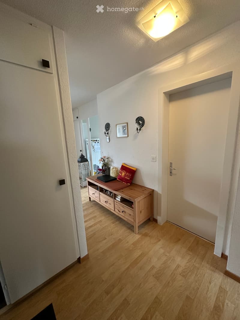 Entrance hall with wooden floor, wooden console table, wall decorations, open door leading to another room