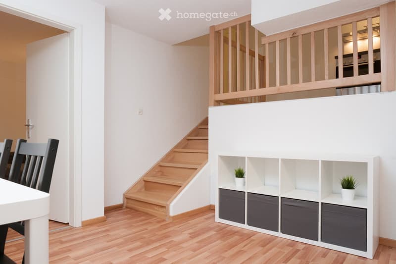 Staircase, wooden floor, white walls, open kitchen, gray storage boxes, table and chairs
