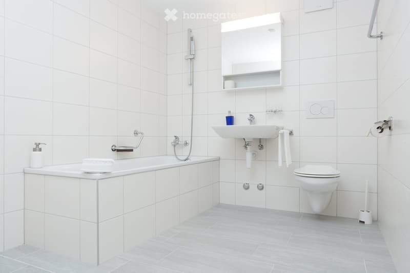 Bathroom: white tiles, bathtub, sink, toilet, mirror, shower head, toiletries, towels