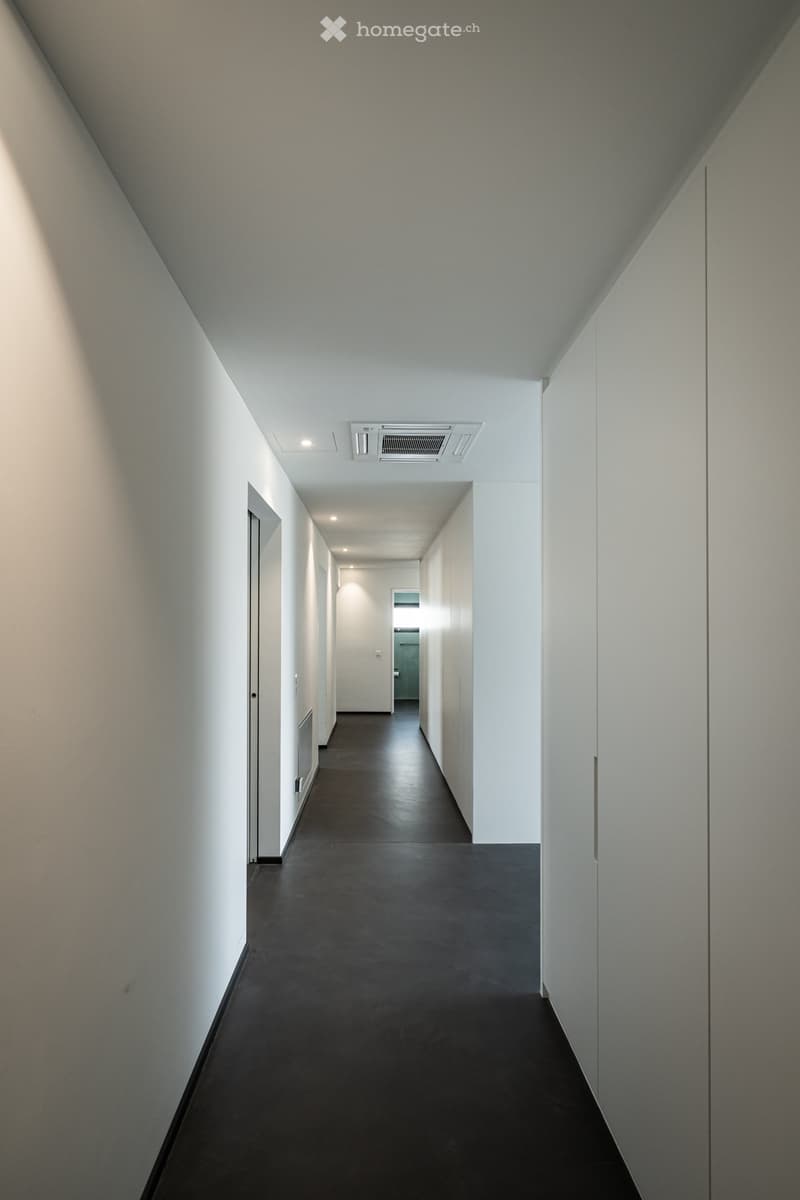Empty hallway with white walls, black floor, and ceiling lights