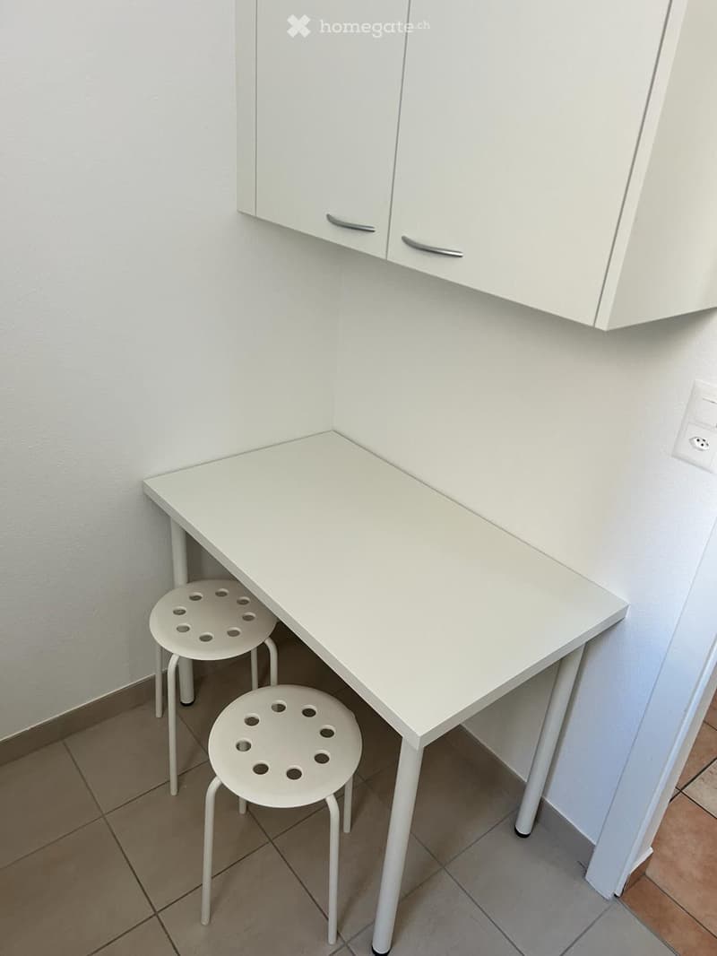 white desk with 2 stools, white wall, cabinets mounted on the wall, tiled floor