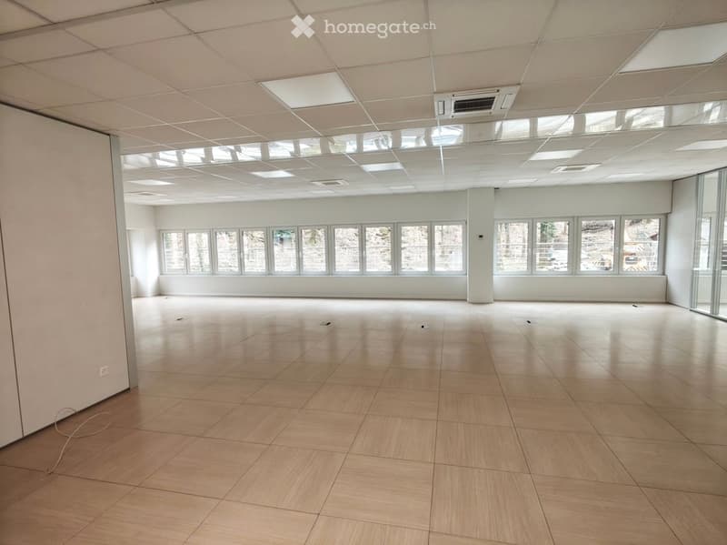 Empty room with white walls, wooden floor, large windows, ceiling with lights and air conditioning units
