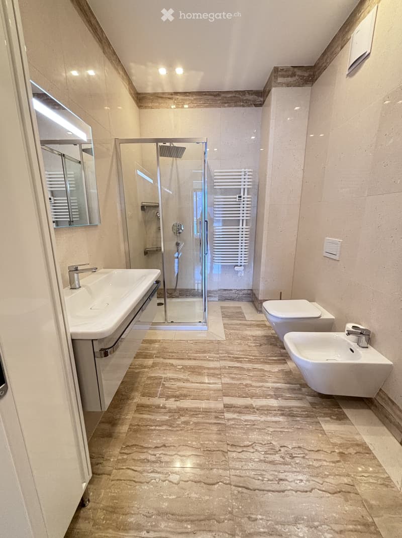 modern bathroom with shower, double sink, two toilets, marble flooring, white walls, large mirror