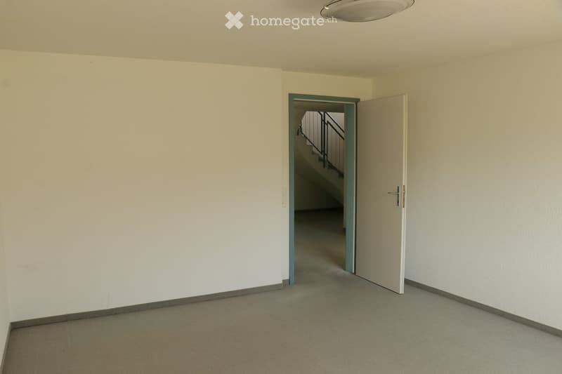 Empty room with white walls, gray floor, open door, and staircase visible