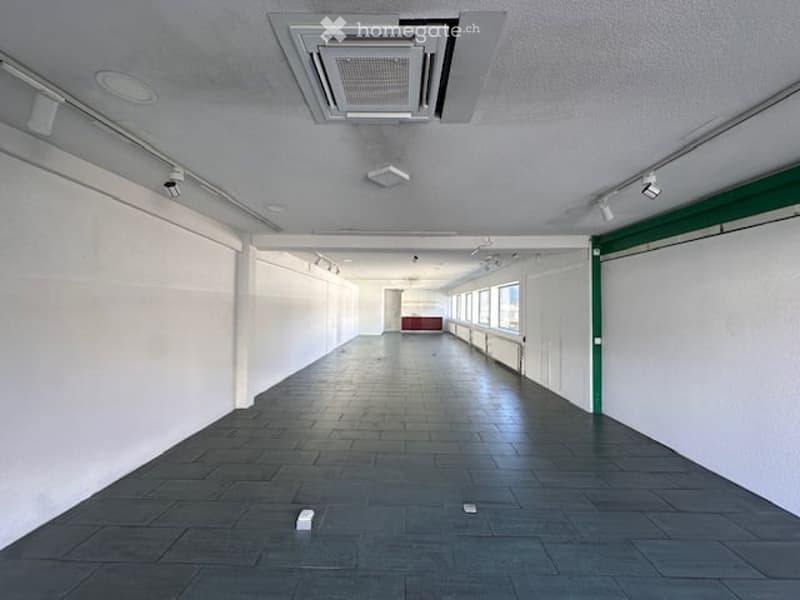 Empty room with white walls, black tiled floor, ceiling with air conditioning unit, track lighting, and windows