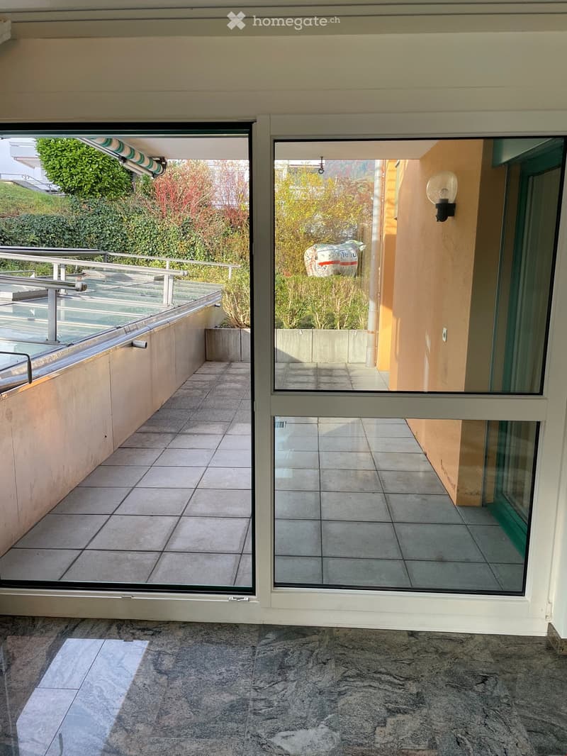 Balcony with sliding glass doors, tiled floor, metal railing, wall lamp, view of greenery