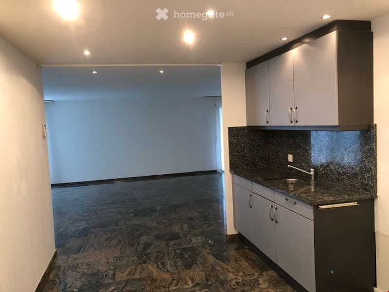 Empty room with marble floor, white walls, kitchen area with sink and cabinets