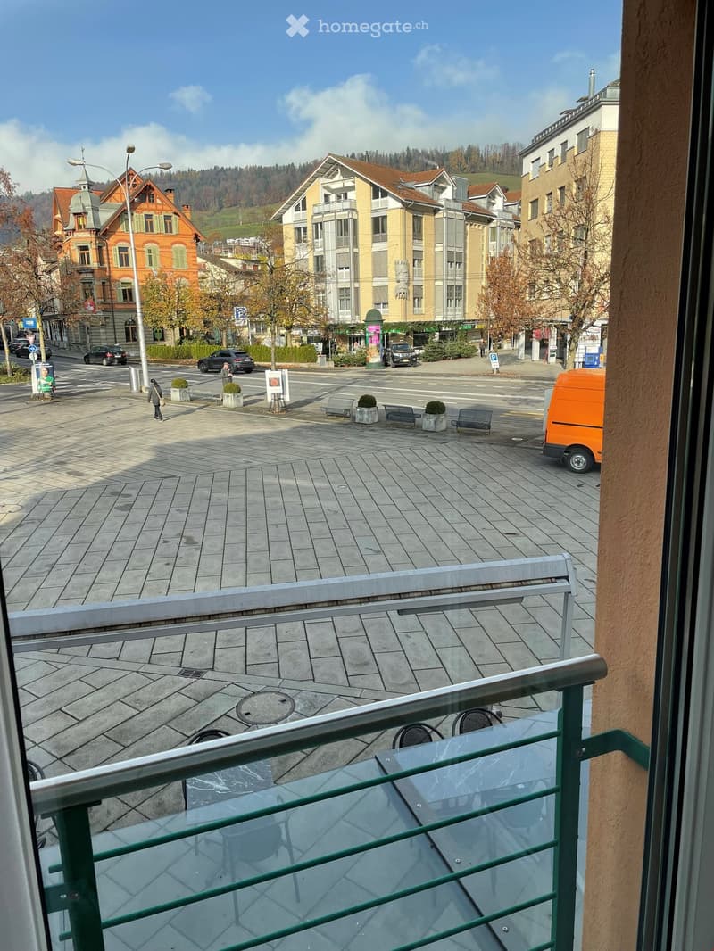 Balcony with table and chairs, view of a street with buildings and people