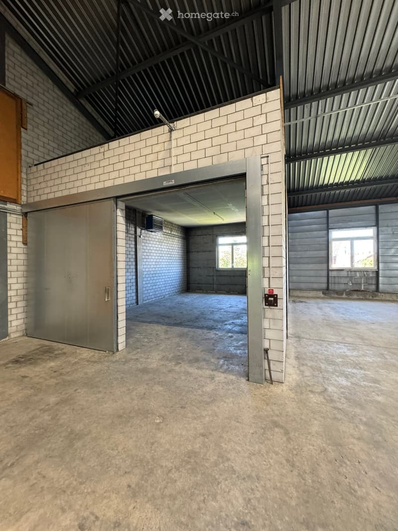 Empty industrial-style room with concrete floor, brick walls, metal ceiling, and large garage door. No furniture or equipment present.