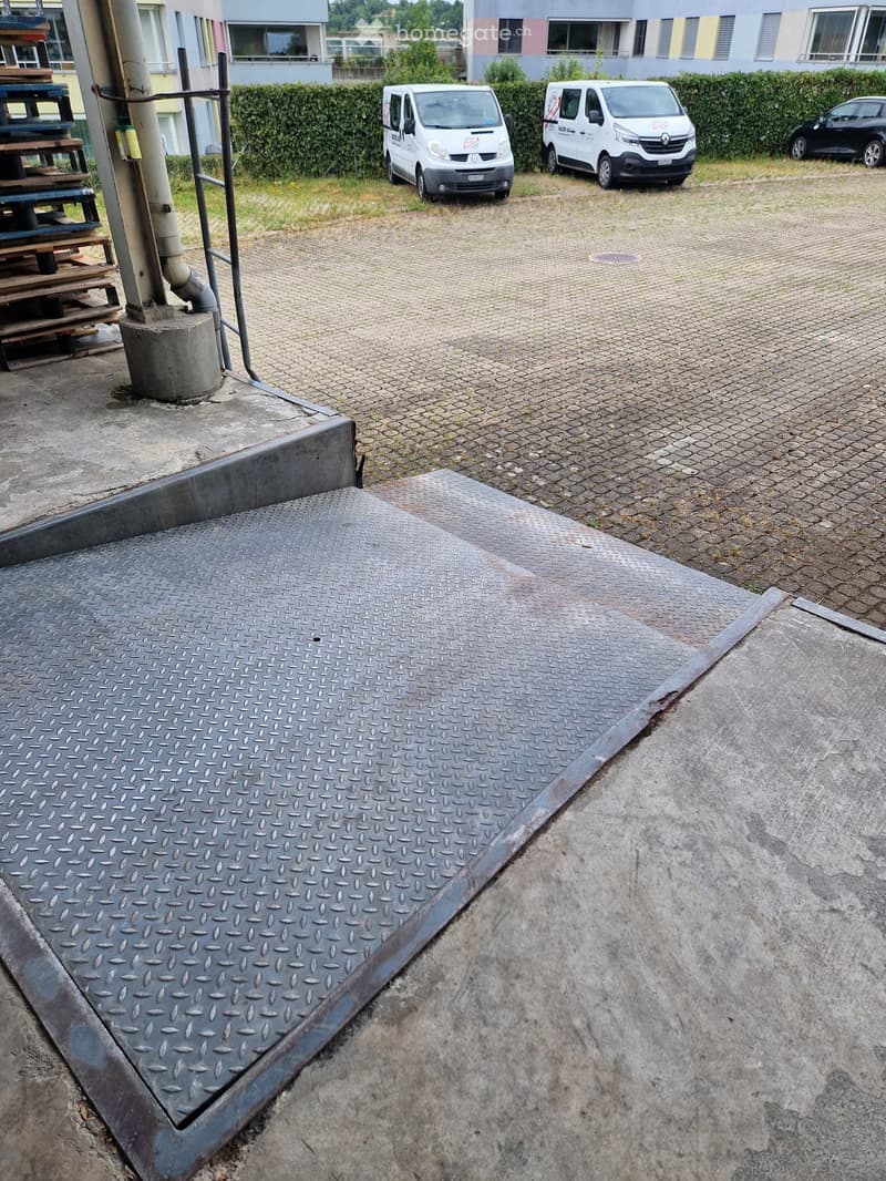 A paved parking area with a metal ramp, two white vans parked, and a building in the background.
