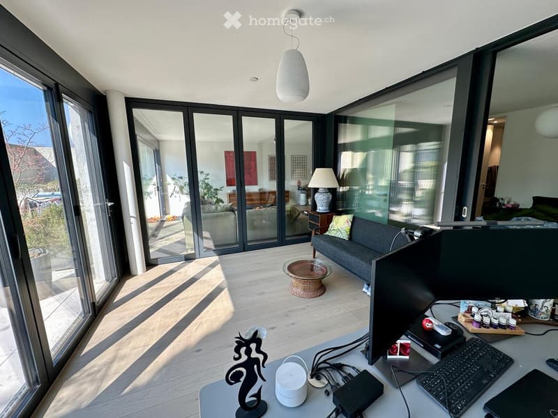 modern living room with sliding glass doors, hardwood floors, large windows, desk with computer, couch, coffee table, lamp, and decorative items