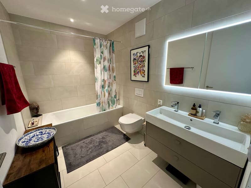 Bathroom with bathtub, toilet, double sink, mirror, towel rack, and tiled floor