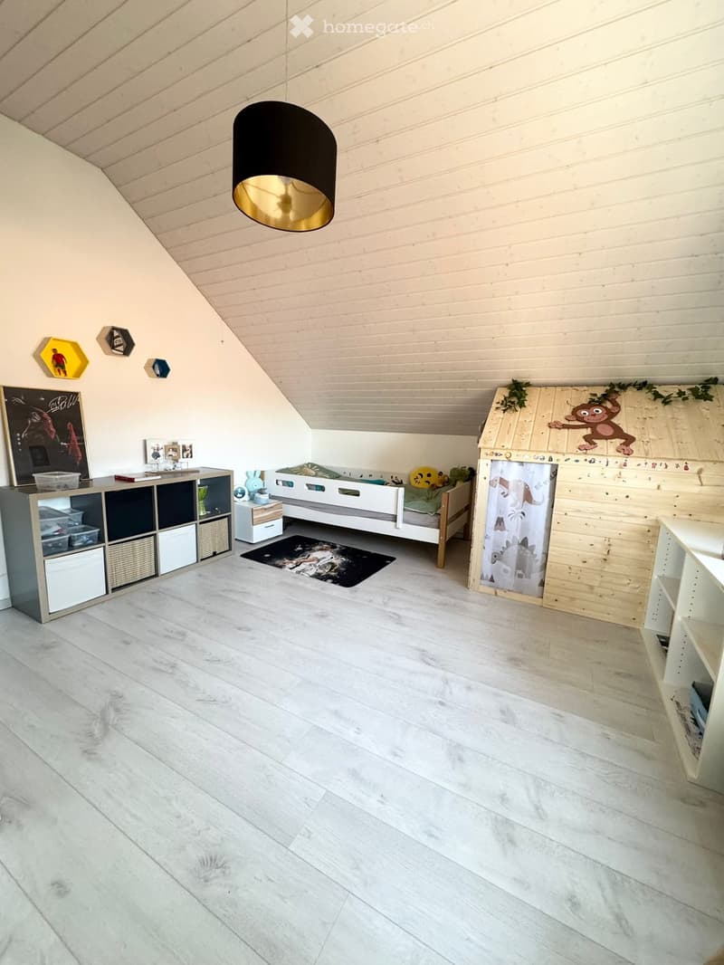 A child's room with a bed, a wooden playhouse, a shelf, a rug, and a lamp