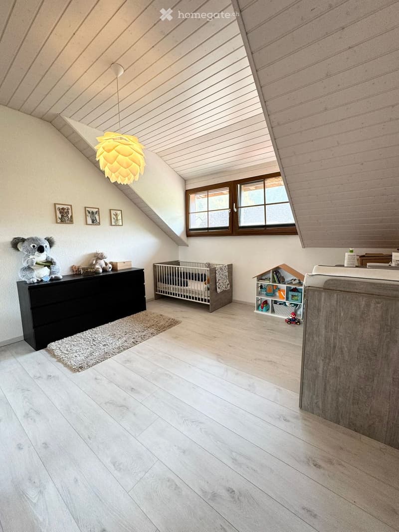 A room with a crib, a black dresser, a rug, a lamp, a toy house, and a window.
