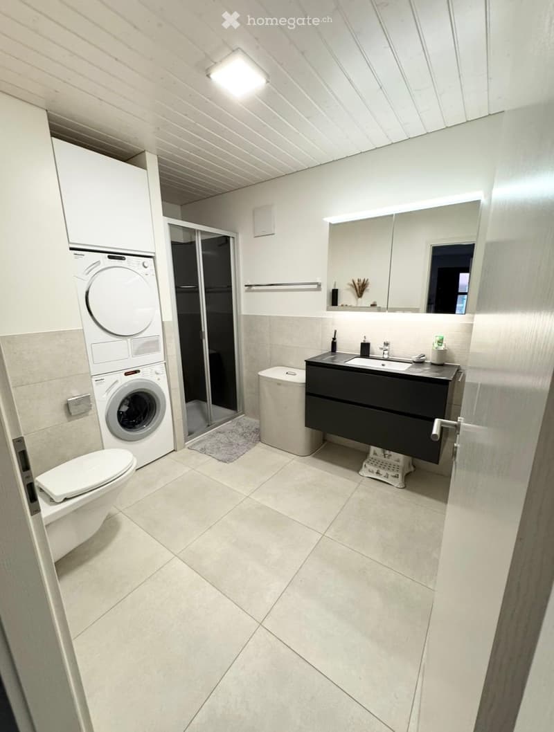 modern bathroom with white tiles, white toilet, white washing machine, black vanity, mirror, shower