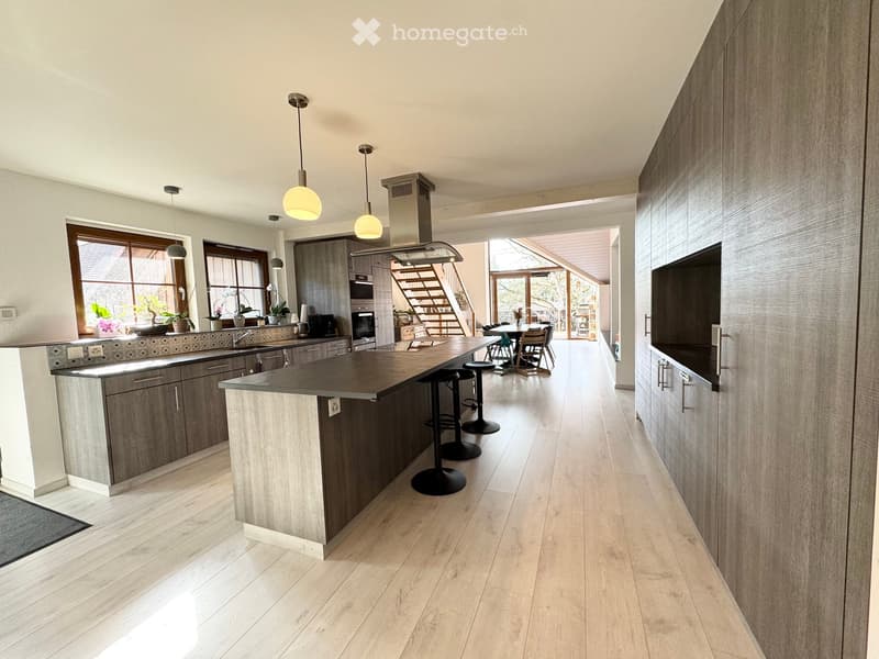 modern kitchen with island, wooden cabinets, granite countertops, stainless steel appliances, pendant lights, hardwood floors, dining area with table and chairs, staircase leading to upper level