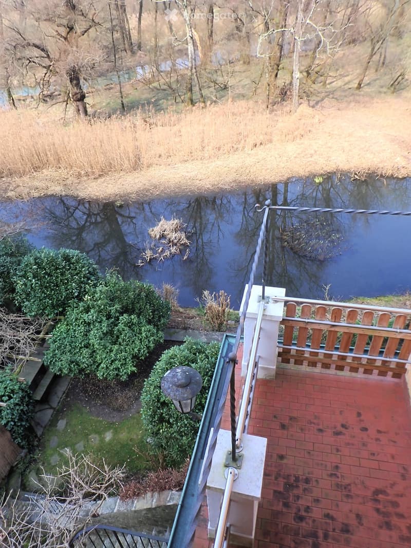 Balcony with railings, brick floor, lamp, shrubs, and a view of a river