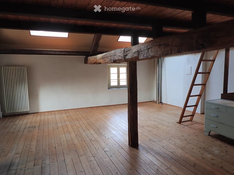 Empty room with wooden floor, wooden beams, white walls, radiator, window, ladder, and a cabinet