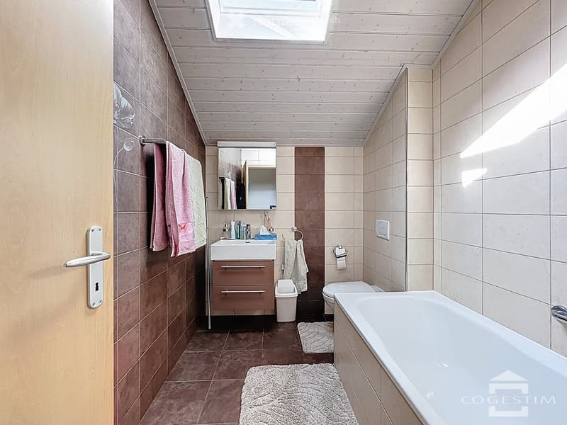Bathroom with bathtub, sink, toilet, mirror, and tiled walls and floor.