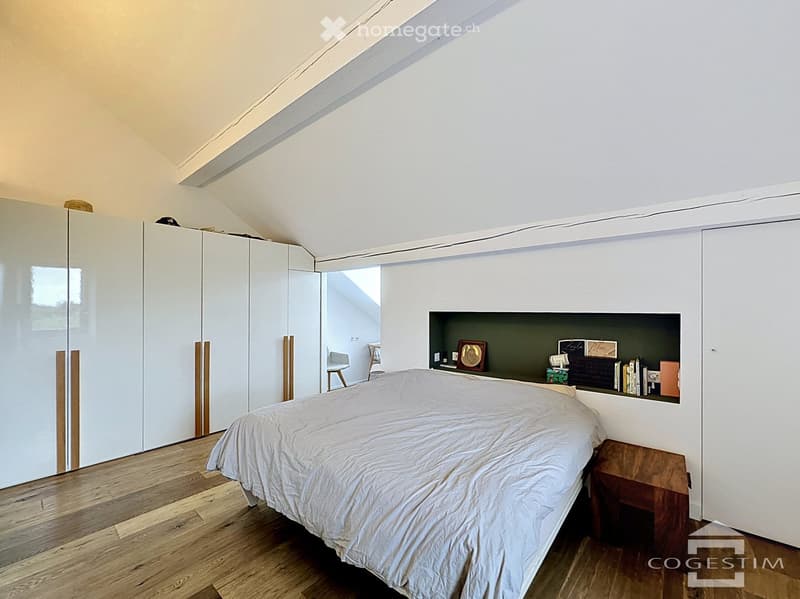 Modern attic bedroom with wooden flooring, white walls, built-in wardrobe, and a built-in shelf unit with decorative items.