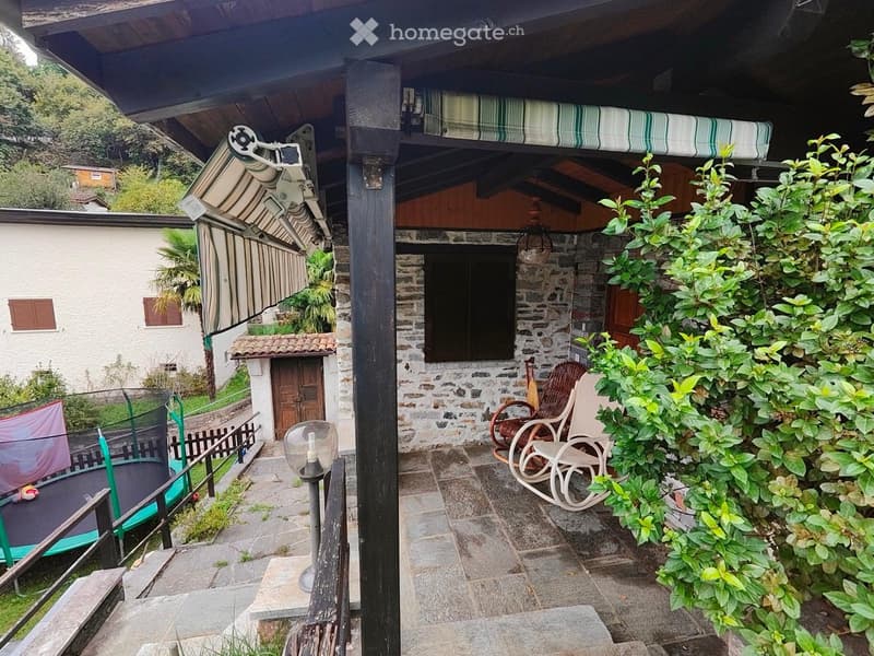 Stone house, wooden porch, awning, outdoor seating, trampoline, garden