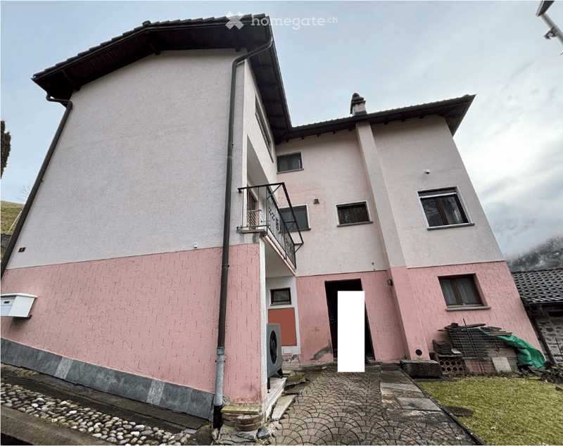 Two-story house with pink and white walls, a balcony on the second floor, a chimney, and a small garden in front.