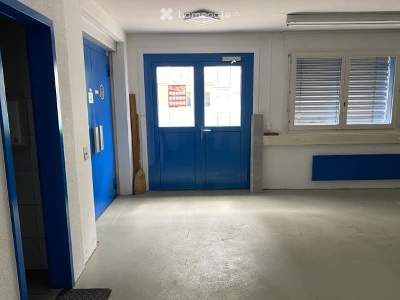 Empty room with blue doors, white walls, concrete floor, and a window with blinds.