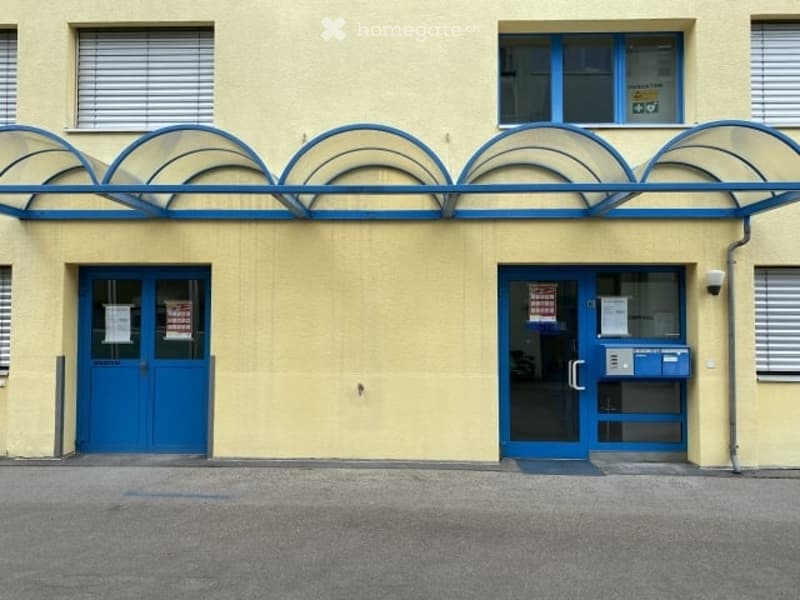 Yellow building with blue doors and windows, glass canopy, two entrances, yellow walls, blue trim, glass windows, metal pipe on the right side