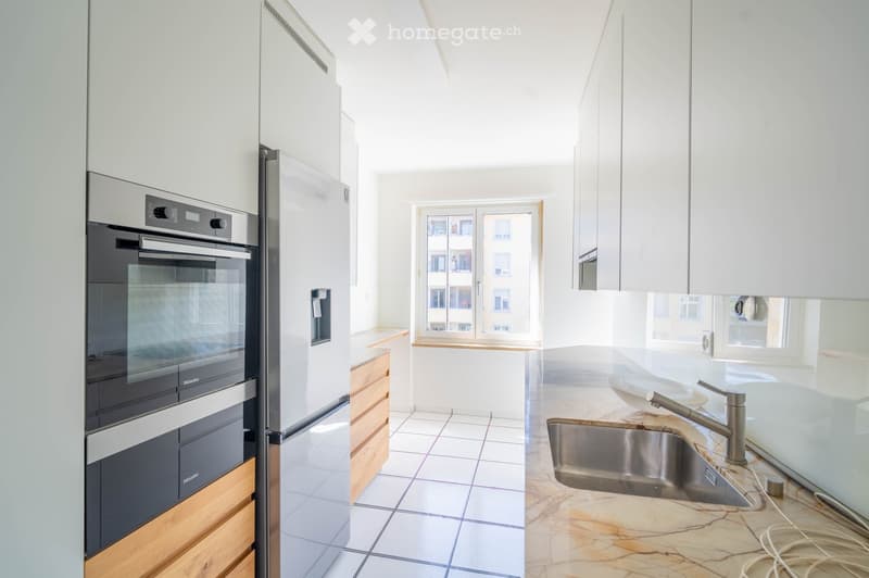 modern kitchen with white cabinets, marble countertop, stainless steel appliances, wooden drawers, white tiled floor, large window