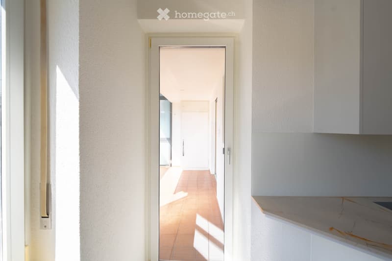 Empty room with white walls, tiled floor, open door, and a view of a hallway.