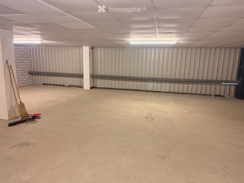 Empty room with concrete floor, white walls, metal beams, and ceiling lights