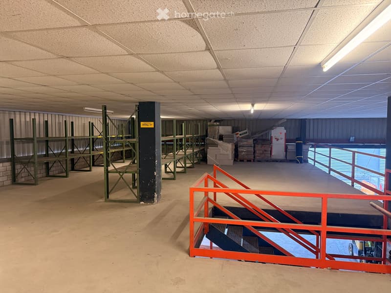 Empty storage room with metal shelves, metal railings, and a forklift visible in the background.