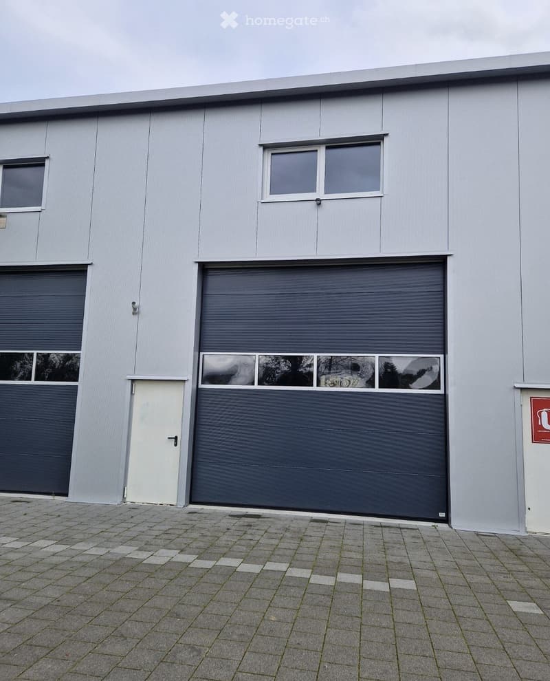 Industrial building with two large garage doors, one smaller white door, and two windows