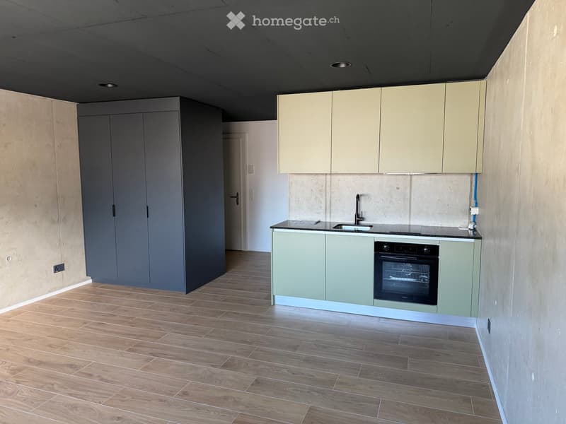 empty room, wooden floor, gray wardrobe, kitchen with sink, oven, and cabinets
