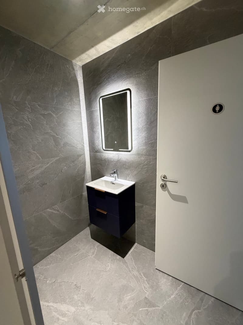 small bathroom with gray tiles, white sink, mirror, and blue cabinet