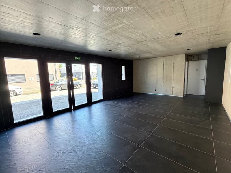 Empty room with black tiled floor, large glass doors, and an exit sign