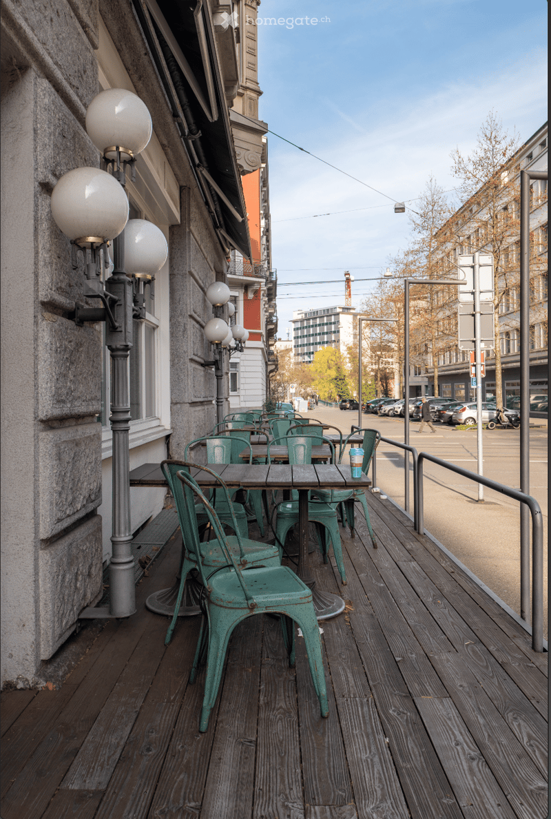 Wooden deck with green chairs and tables, street lamps, and a view of the street