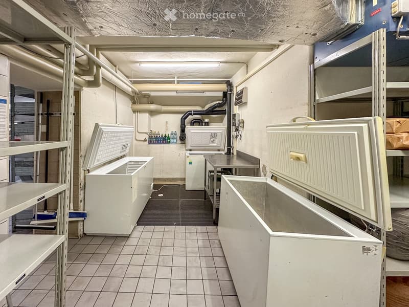 Storage room with white freezers, shelves, tiled floor, metal table, and various equipment