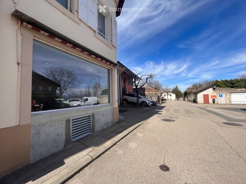 Building with a glass storefront, white shutters, and a garage with cars parked in front.