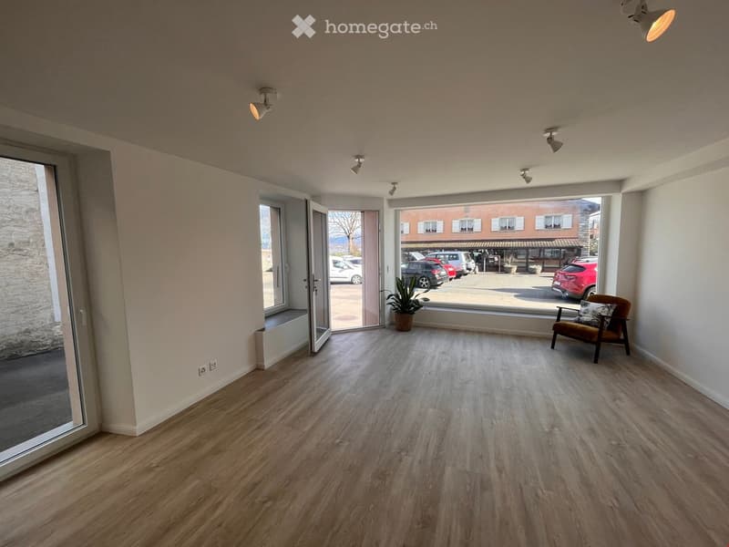 large room, wooden floor, white walls, large windows, plants, chair, open doors